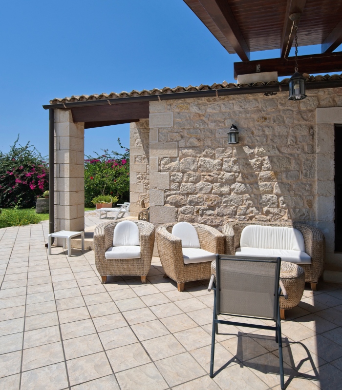 Terrasse carrelée extérieure devant maison en pierre avec salon de jardin