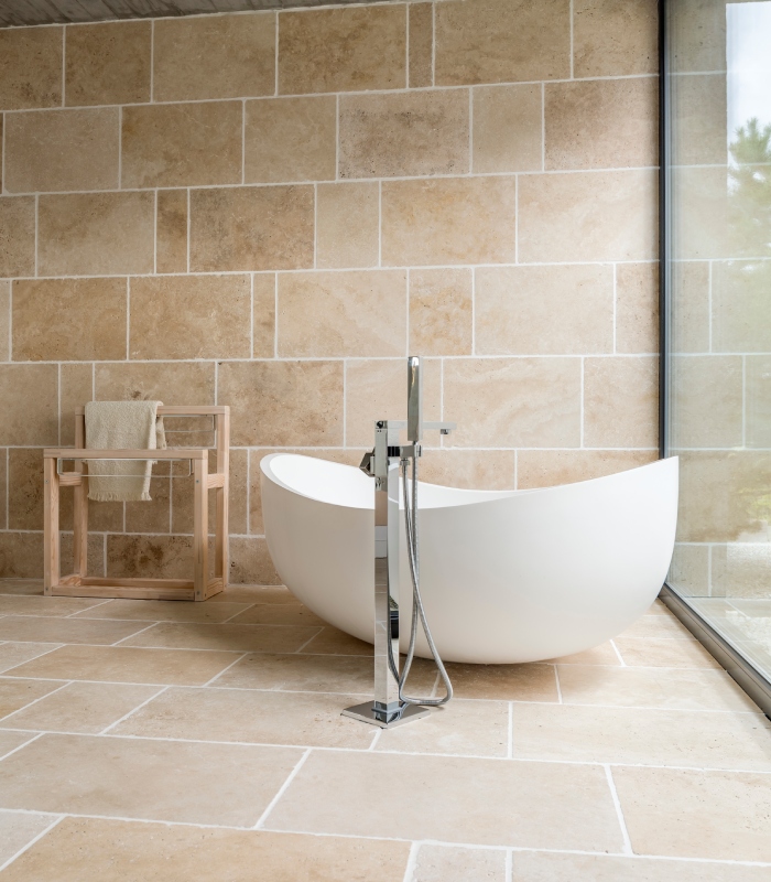 Salle de bain avec carrelage en pierre naturelle au sol et murs et baignoire îlot